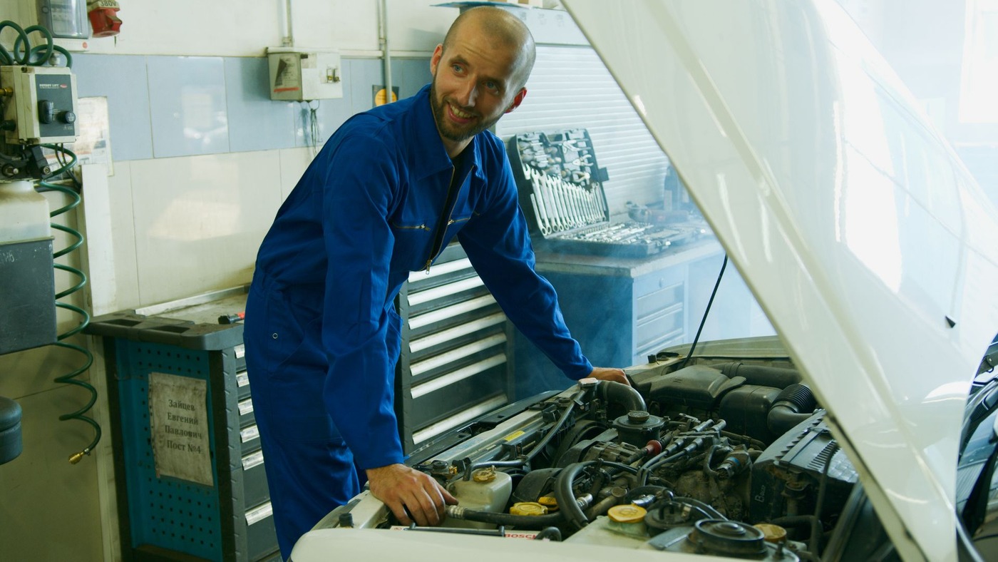 A mechanic leaning over an open engine bay in a repair shop