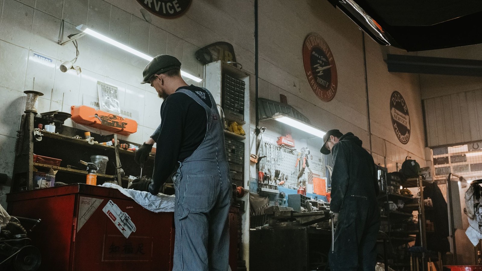 Two mechanics working at benches in a well-used vehicle repair workshop
