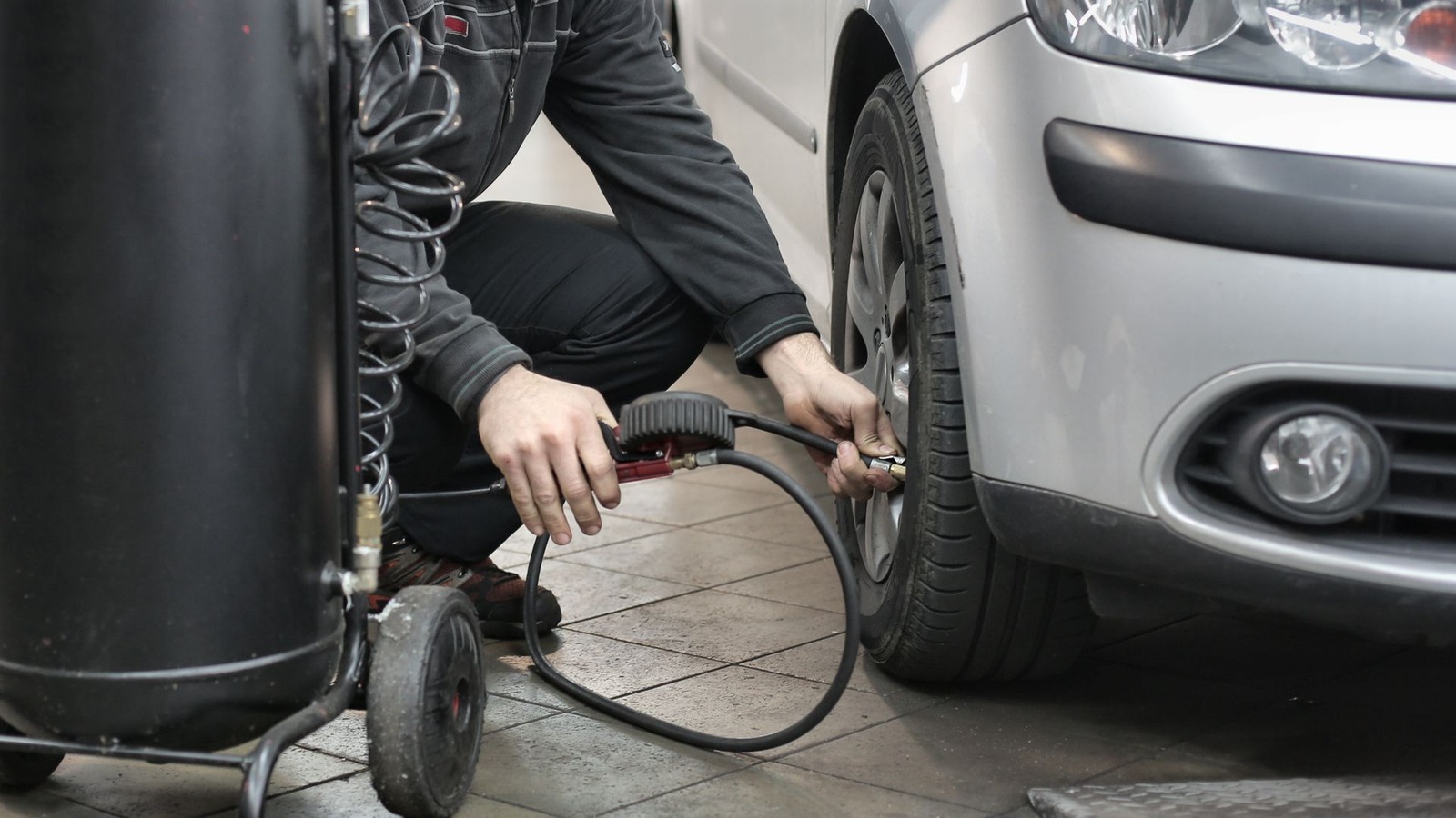 A technician checking a tire with an air line beside a car in a workshop