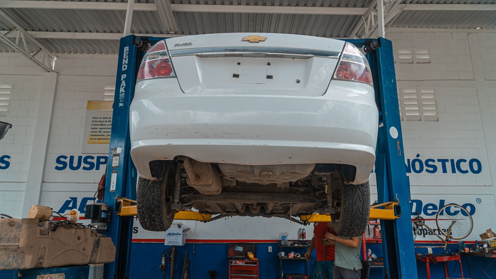 A white sedan raised on a two-post lift in a service bay