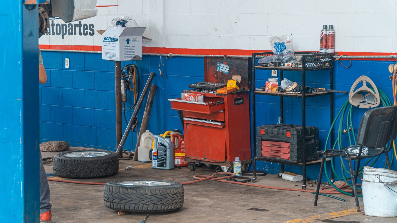 The interior of a vehicle workshop with tool chests, tires and equipment along the wall