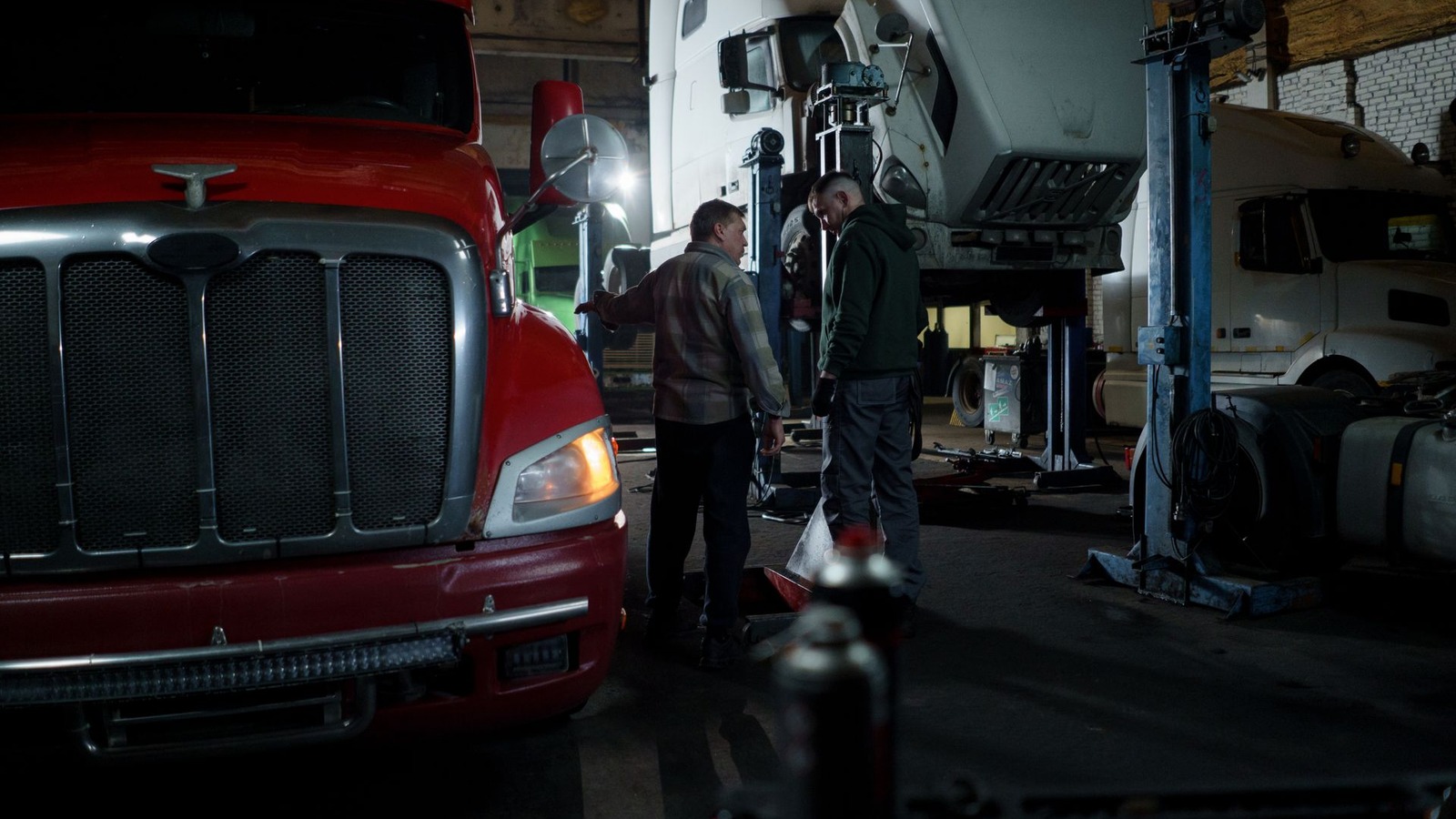 A heavy truck parked in a workshop bay with technicians working nearby