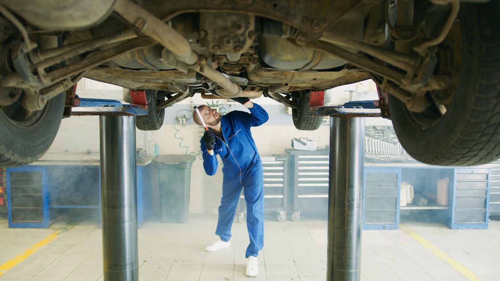 A vehicle raised high on a lift with a technician working underneath it