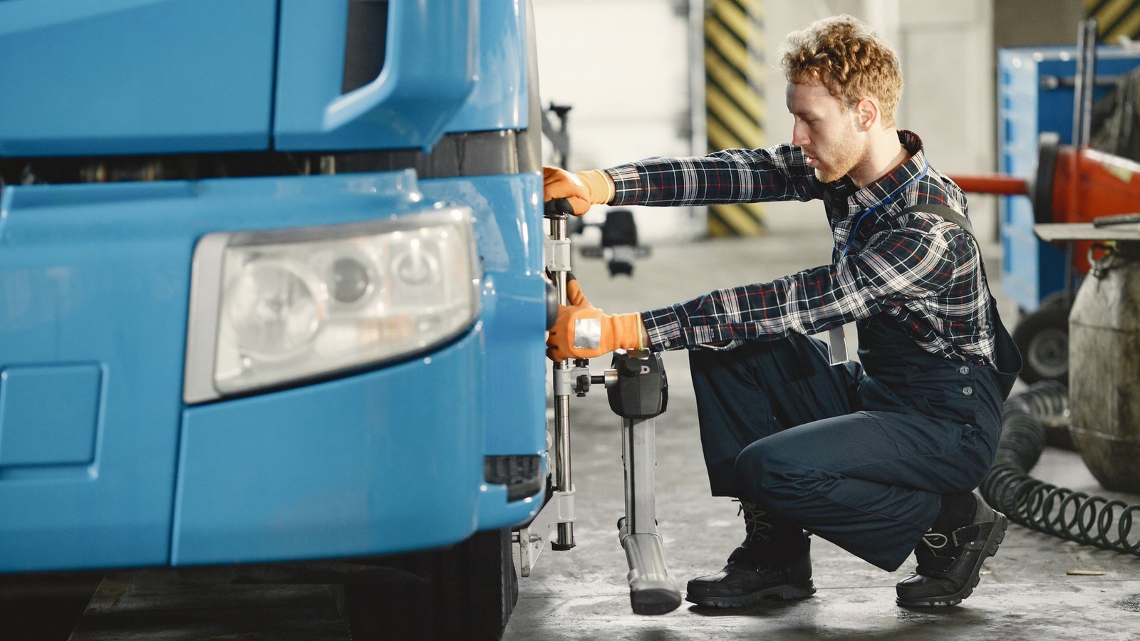 A technician working at the front of a large blue truck in a workshop