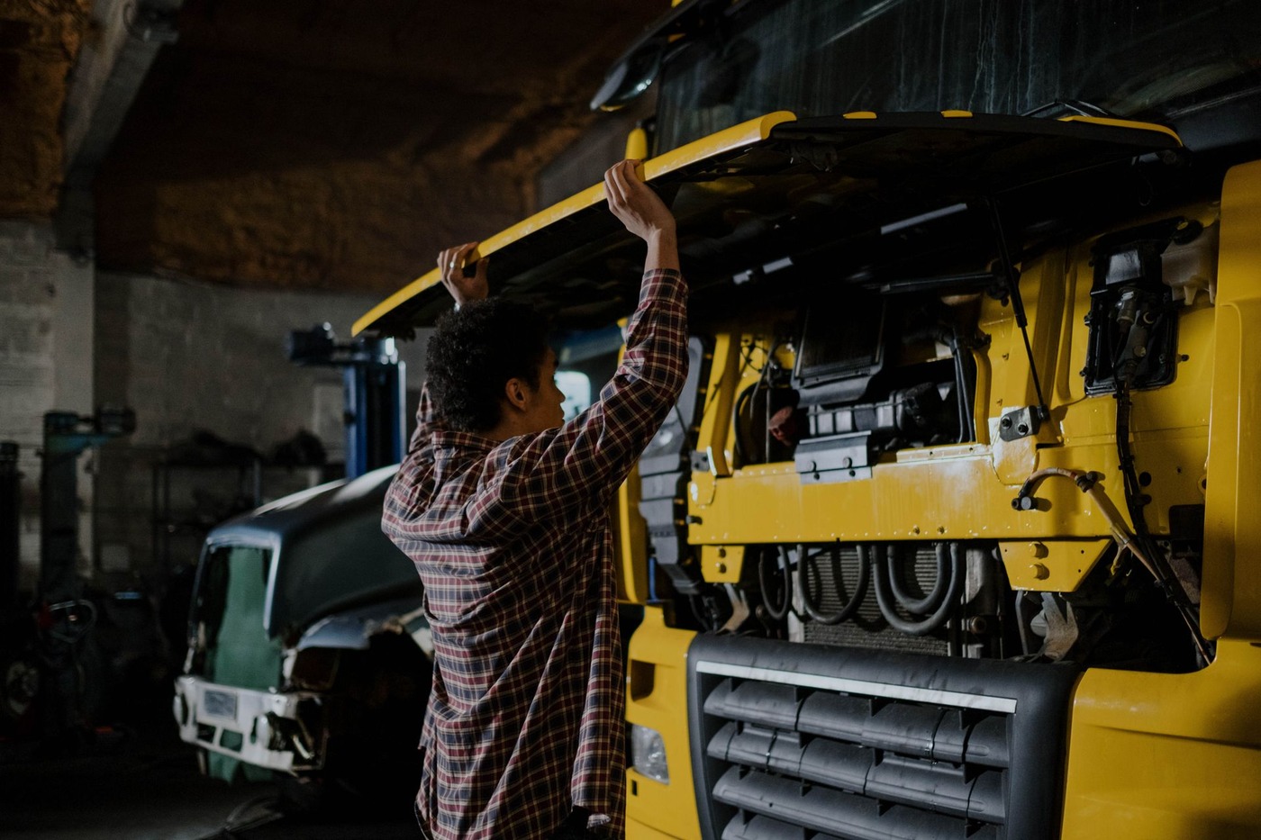 A heavy truck raised on a workshop lift with a technician working beneath it